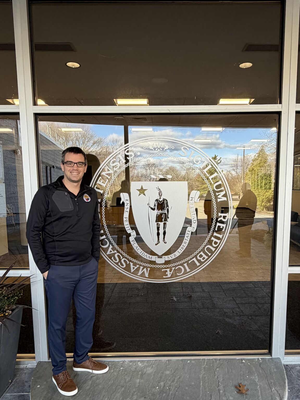Joey Aberle standing in front of a State of Massachusetts logo.